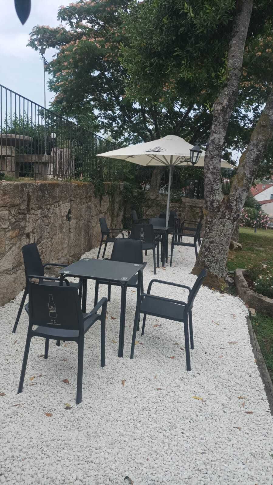 An outdoor seating area with tables and chairs, a large umbrella, and a stone wall.