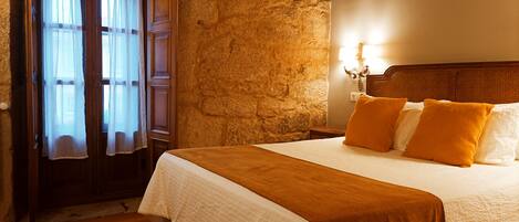 A bedroom with a stone wall, wooden door, and a bed with white and orange bedding.