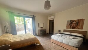 Une chambre avec deux lits, une grande fenêtre avec des rideaux, une table de chevet, une lampe et un tableau au mur.
