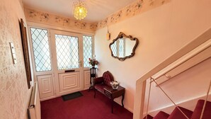 Ein Zimmer mit Treppe, einer Glastür, einem Spiegel und einem kleinen Tisch mit Blumen.