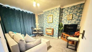 Ein Wohnzimmer mit einer Couch, einem Fernseher, einem kleinen Tisch und einer Wand mit Muster.