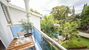 Un balcon avec un banc en bois, des plantes en pot et une vue sur une piscine entourée d’une végétation luxuriante.