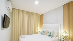 Une chambre d’hôtel avec un grand lit, un téléviseur à écran plat fixé au mur, une table de chevet avec une lampe et une fenêtre avec des rideaux.