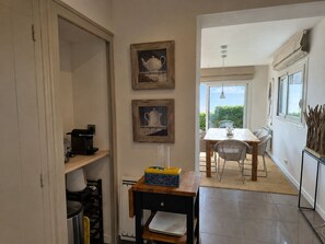 Un couloir étroit mÚne à un espace repas comprenant une table et des chaises, une petite table sur laquelle se trouve une boßte, et des tableaux encadrés accrochés au mur.