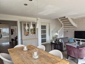 Ein modernes Wohnzimmer mit einem Holzesstisch, weißen Korbstühlen, einem grauen Sofa und einer Treppe.