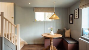 A cozy room with a wooden staircase, a round wooden table with a vase, a bench with cushions, and a window with blinds. - Boutique Cottage in the Heart of Kintbury. Pet friendly! (Kintbury)