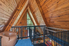 Ein Dachzimmer aus Holz mit schrägen Wänden, einem schwarzen Metallgeländer und einem braunen Ledersessel.