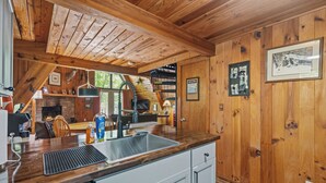 Interior de una cabaña de madera con cocina, comedor y chimenea.