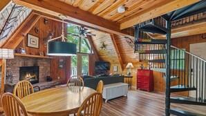 Interior acogedor de una cabaña con comedor, chimenea, techo de madera y una escalera en espiral.