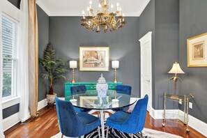 A dining area with a glass table surrounded by blue chairs, a chandelier, a potted plant, and a blue cabinet with a decorative vase. - The Majestic Fern (Savannah)