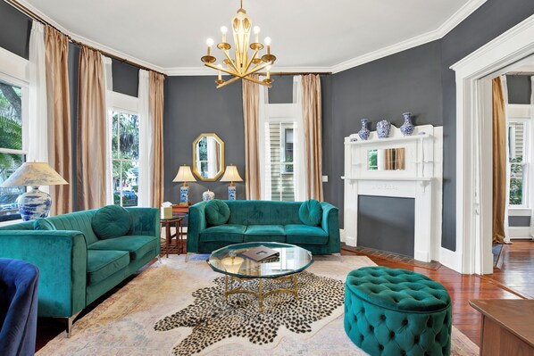 A living room with a teal sofa, a glass coffee table, and a fireplace. - The Majestic Fern (Savannah)
