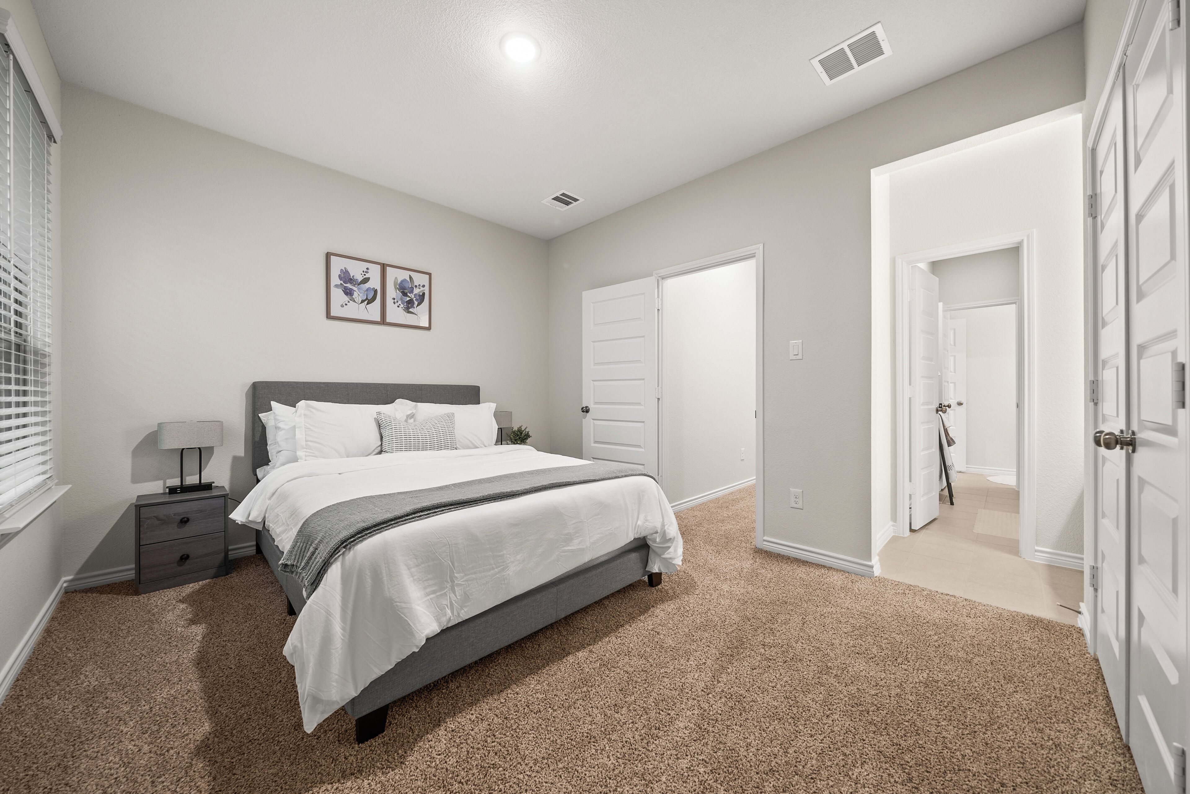 A bedroom with a bed, nightstand, and a door leading to another room.