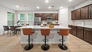 Een moderne keuken met een centraal eiland, donkere houten kastjes, roestvrijstalen apparatuur en een eetgedeelte met barstoelen.