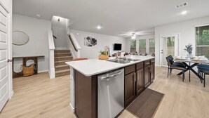 Een moderne keuken met een centraal eiland, inbouwapparatuur en een eethoek met een tafel en stoelen.