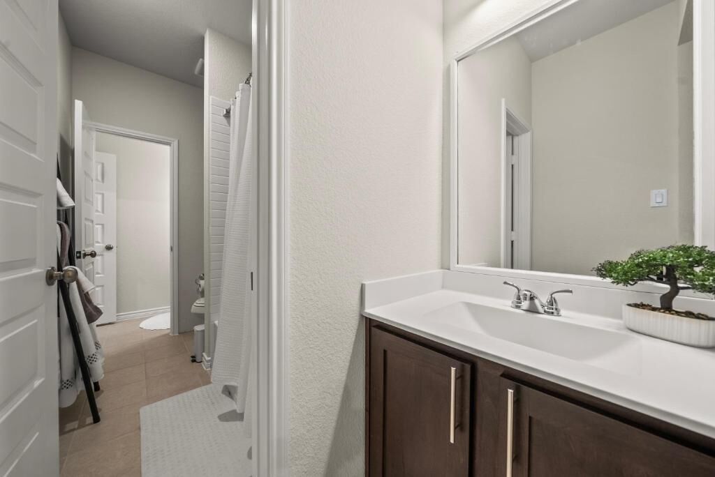 Un baño con lavamanos blanco, armarios de madera oscura, un espejo grande y una planta en maceta.