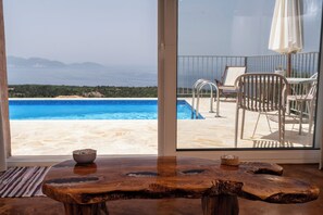 Ein Holztisch mit Schüssel und Kerze, Blick auf einen Swimmingpool und eine Terrasse mit Stühlen und Sonnenschirm.