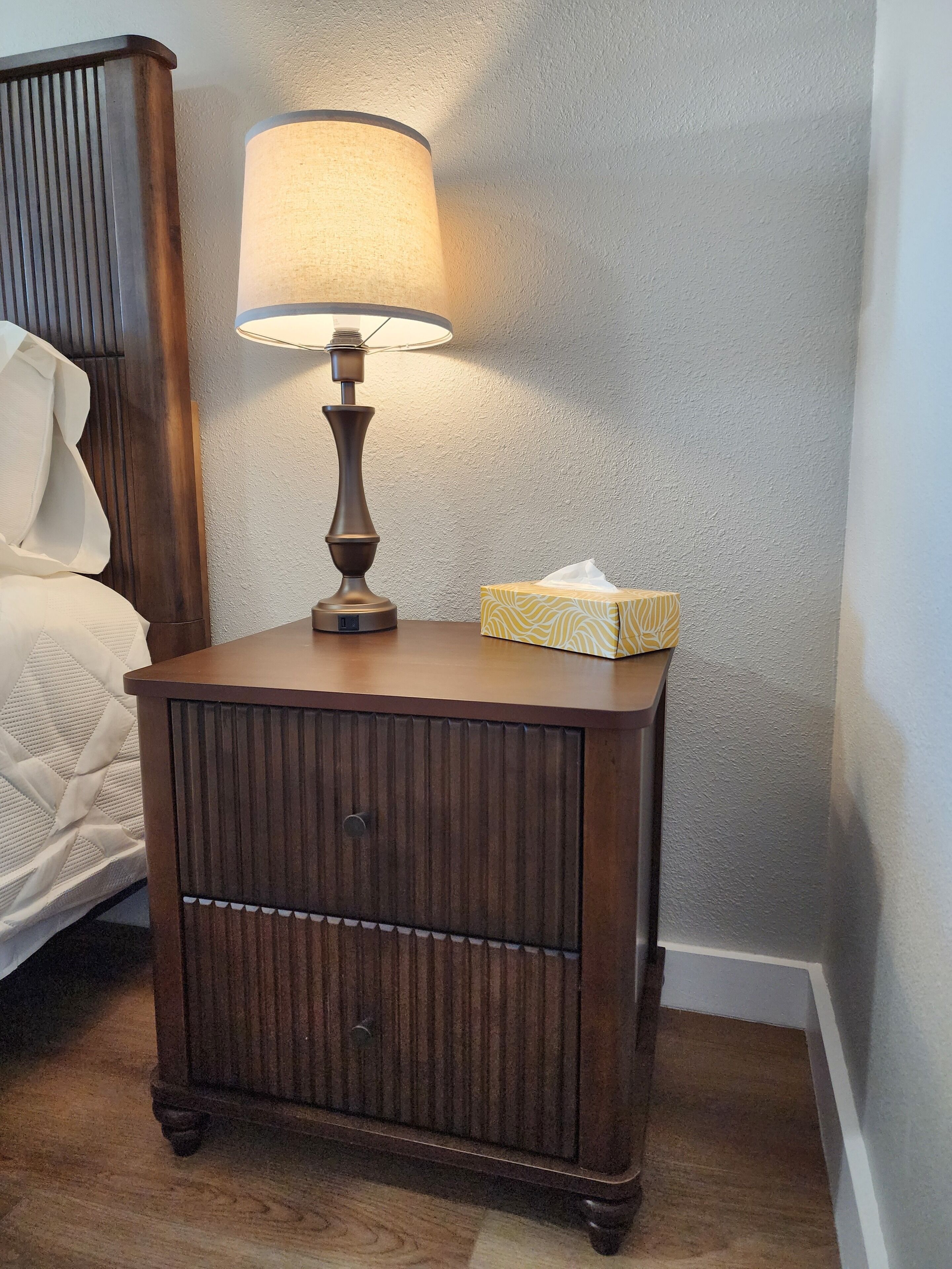 A wooden bedside table with a lamp and a tissue box.