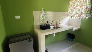 Uma cozinha compacta com pia, um cesto de lixo pequeno e uma geladeira compacta.