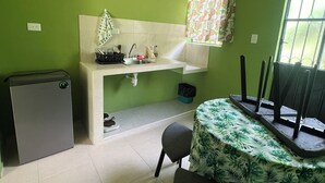 Uma cozinha compacta com pia, um pequeno refrigerador e uma mesa com toalha de mesa estampada com folhas.