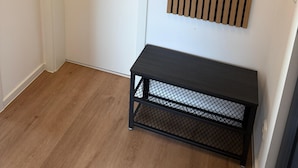 Huone, jossa on valkoinen ovi, musta metallinen penkki ja puulankkuja sisältävä seinäpaneeli.