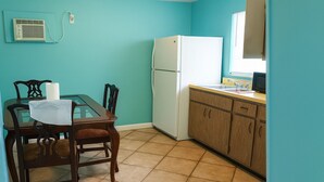 Une cuisine de taille réduite avec des murs de couleur turquoise, un réfrigérateur blanc, des armoires en bois et une table à manger avec des chaises.