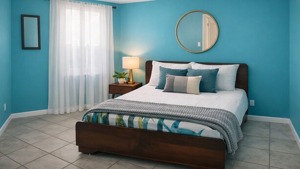 Une chambre à coucher avec un lit, une table de chevet, une lampe, un miroir et une fenêtre avec des rideaux.