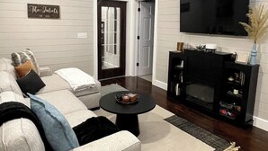 A modern living room with a sofa, a coffee table, a fireplace, and a mounted TV. - Cozy 3-bedroom house with exquisite attention to detail! (Adair)