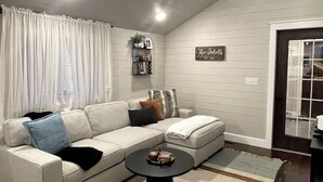 A cozy living room with a sectional sofa, a coffee table, and a decorative wall sign. - Cozy 3-bedroom house with exquisite attention to detail! (Adair)