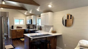 A modern kitchen with wooden beams, white cabinetry, and a central island with stools. - Cozy 3-bedroom house with exquisite attention to detail! (Adair)