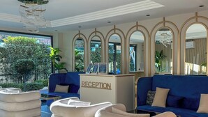 A reception area with a reception desk, blue sofas, and white poufs. - Аpartment 1+1 Qoople Triumph 17 next to Cleopatra Beach (Alanya)