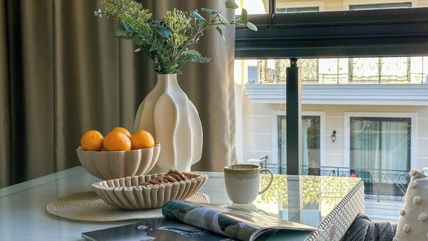 A table with a bowl of oranges, a vase with greenery, and a cup. - Аpartment 1+1 Qoople Triumph 17 next to Cleopatra Beach (Alanya)
