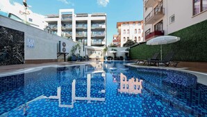 A swimming pool with a tiled floor, surrounded by buildings, some with balconies. - Аpartment 1+1 Qoople Triumph 17 next to Cleopatra Beach (Alanya)