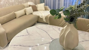 A living room with a beige sofa, a round marble coffee table, and a vase with green foliage. - Аpartment 1+1 Qoople Triumph 17 next to Cleopatra Beach (Alanya)