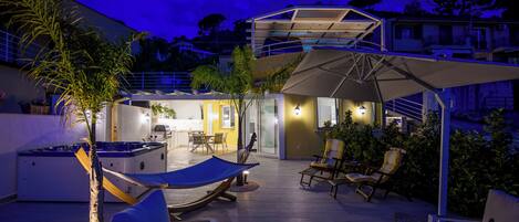 A rooftop patio with a hammock, seating, and a hot tub.