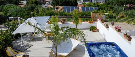 A rooftop terrace with a hot tub, lounge chairs, and potted plants.