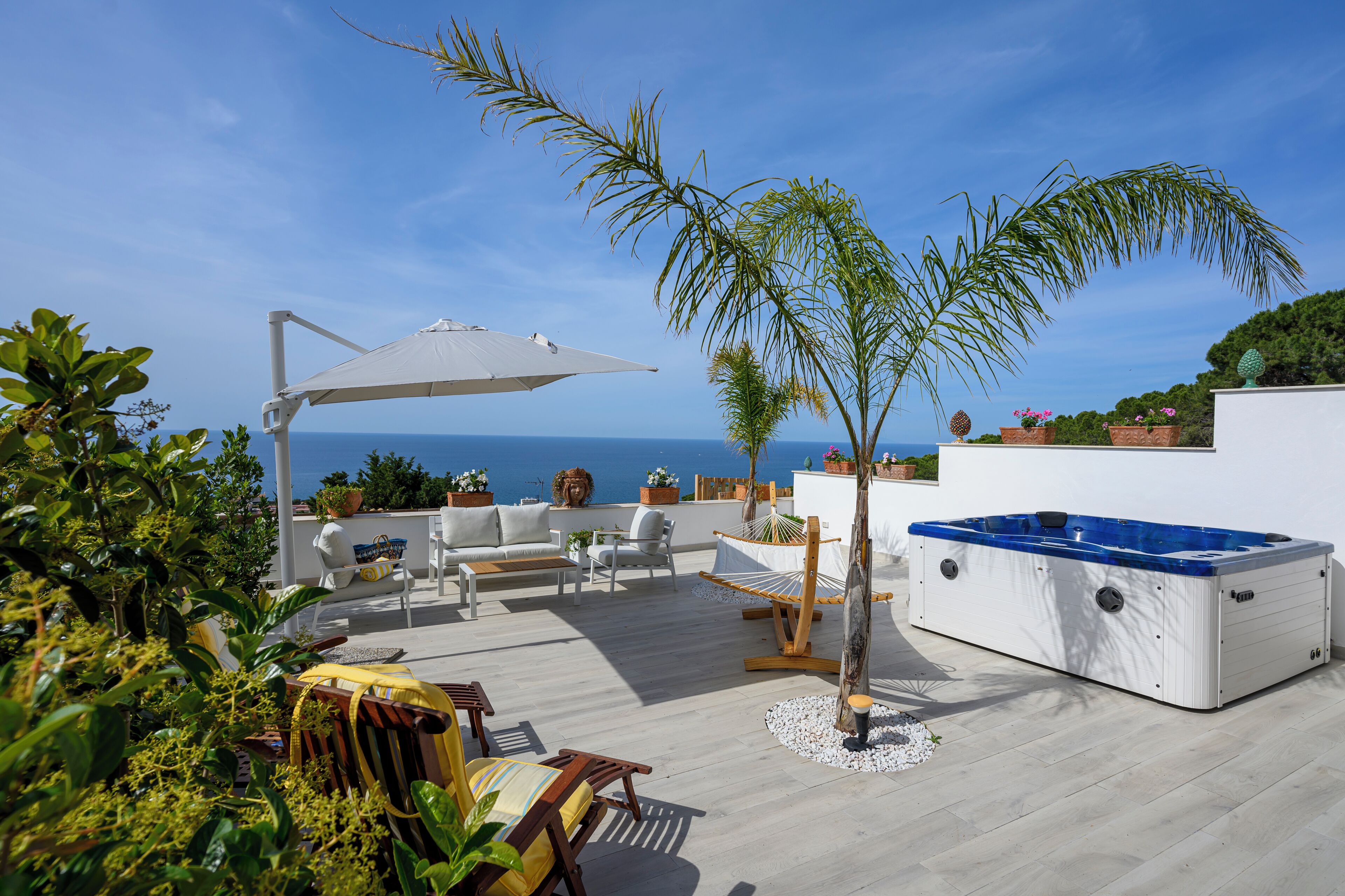 A rooftop terrace with a hot tub, outdoor furniture, and potted plants.