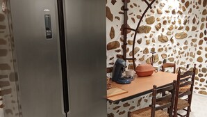 Una cocina con un refrigerador de acero inoxidable, una mesa de comedor con sillas y una pared con diseño de piedra.