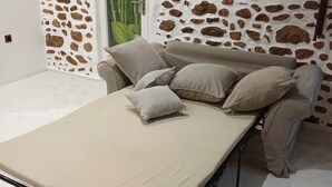 Una cama con colchón y almohadas, una pared de piedra y una puerta con cortina verde.