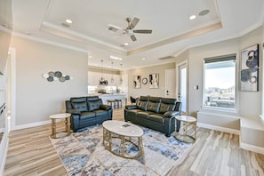A spacious living room with a ceiling fan, two black leather sofas, a coffee table, and a kitchen in the background. - Blissful Blue Oasis- Waterfront in Treasure Island (Freeport)