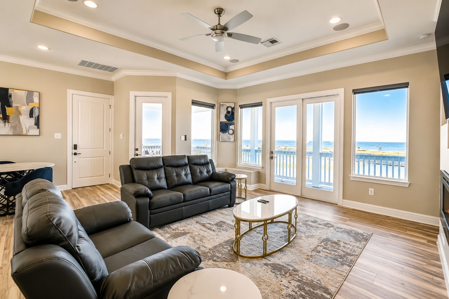 A spacious living room with a large black leather sofa, a coffee table, and a ceiling fan.