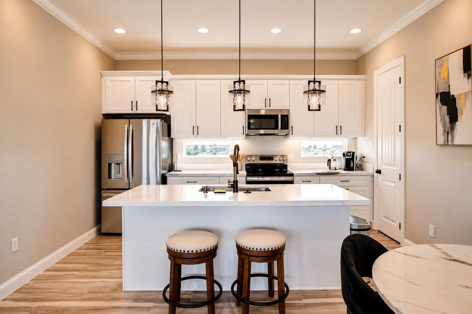 A modern kitchen with white cabinetry, stainless steel appliances, and a central island with stools.