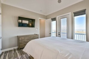 A bedroom with a large bed, a TV on the wall, a dresser, and a balcony with a view of the beach. - Blissful Blue Oasis- Waterfront in Treasure Island (Freeport)