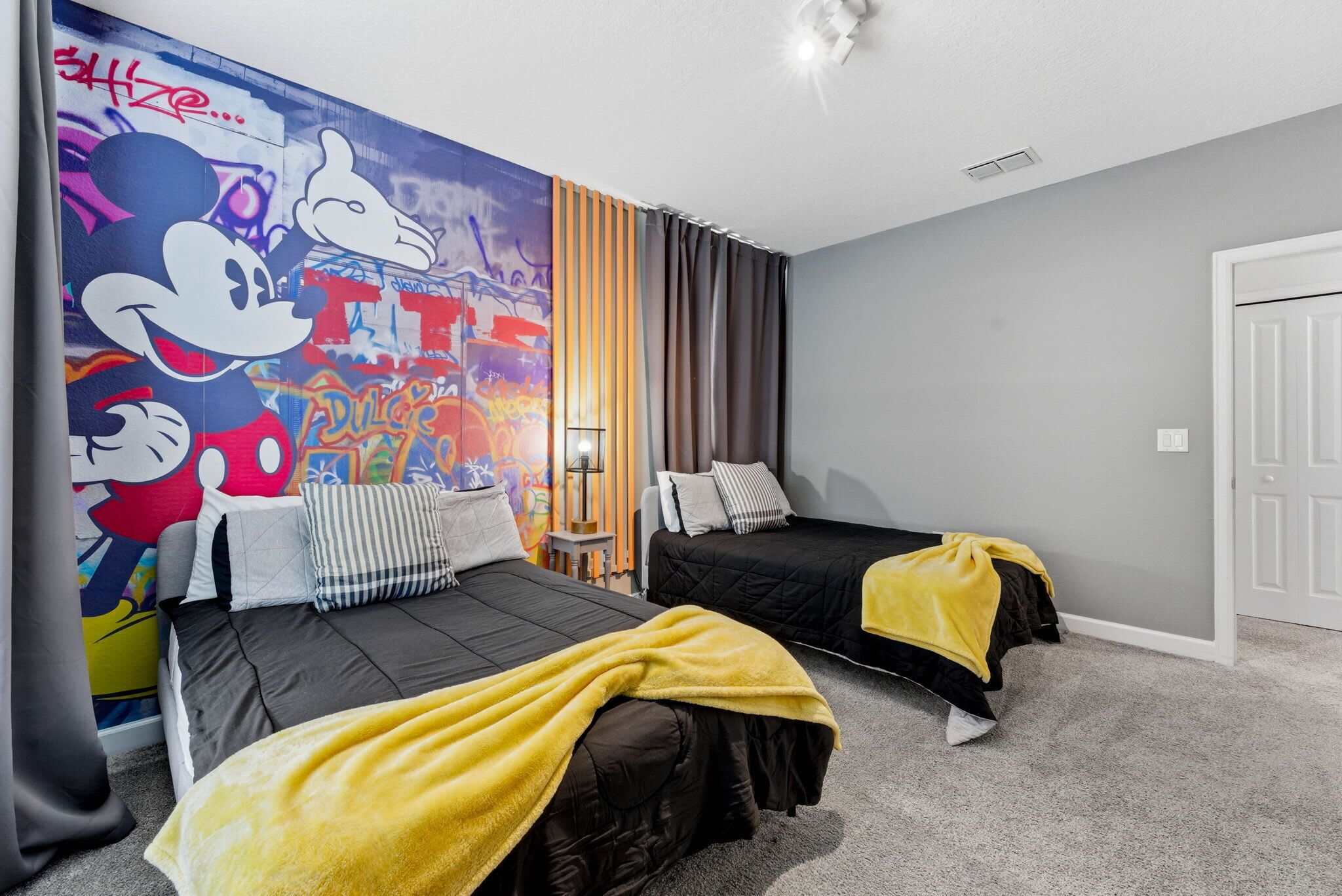 Une chambre d’hôtel avec deux lits, une fresque murale représentant des personnages de dessins animés, une lampe et une porte.