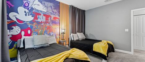 Une chambre d’hôtel avec deux lits, une fresque murale représentant des personnages de dessins animés, une lampe et une porte.