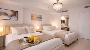 A hotel room with two beds, a chandelier, artwork on the walls, and a breakfast tray with fruit and juice. - Luxe Brickell • 35th Floor • Skyline View • Free Spa & 5 Star Hotel Amenities (Miami)