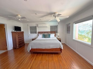 Une chambre avec un lit en bois, deux ventilateurs de plafond, une télévision, une commode et une fenêtre donnant sur un beau paysage.