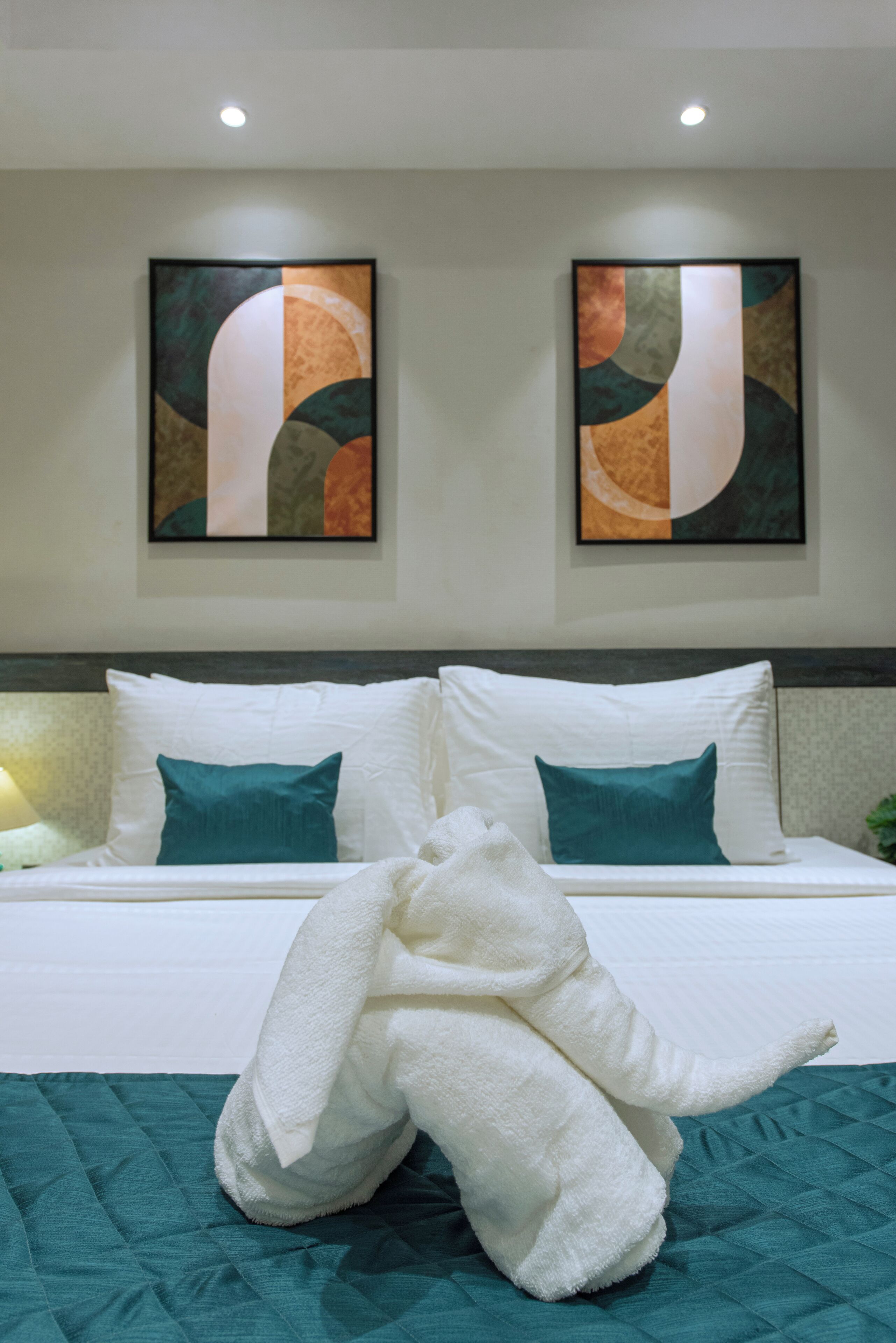 Habitación de hotel con una cama, dos almohadas, una colcha y dos cuadros abstractos en la pared.