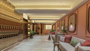 A spacious lobby with a marble floor, a sofa with cushions, potted plants, and a wall with clocks. - Kzar Park (Kolkata)