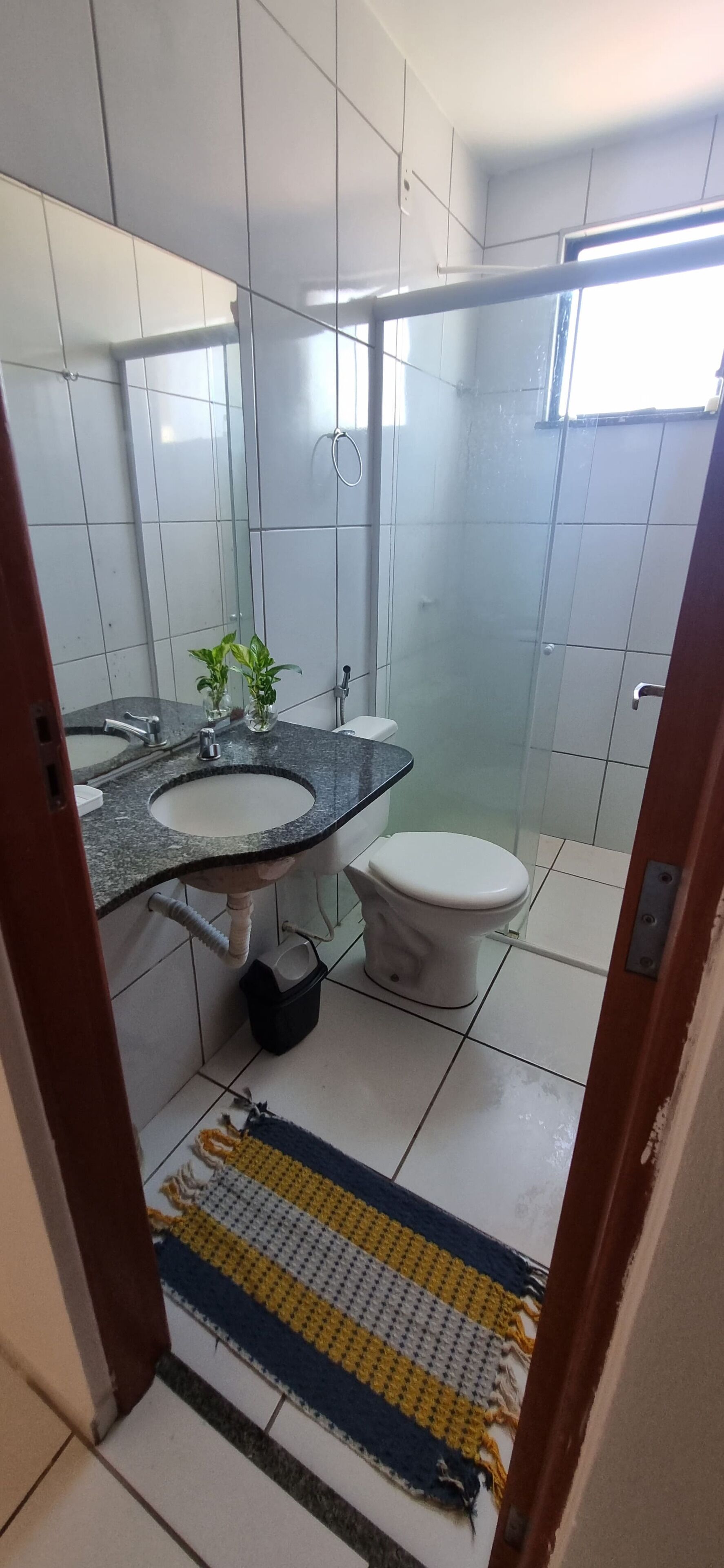 Casa de banho com lavatório, espelho, sanita e chuveiro.