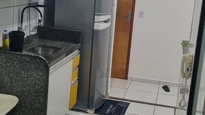 Kompakti keittiö, jossa on valkoiset kaapit, graniittitaso, ruostumattomasta teräksestä valmistettu jääkaappi ja puuovi.